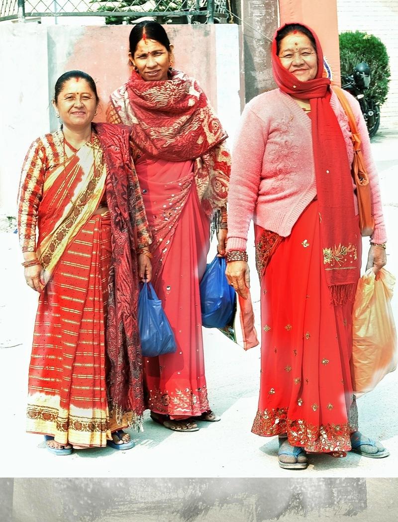 Kolme nepalilaista naista punasävyisissä vaatteissa.