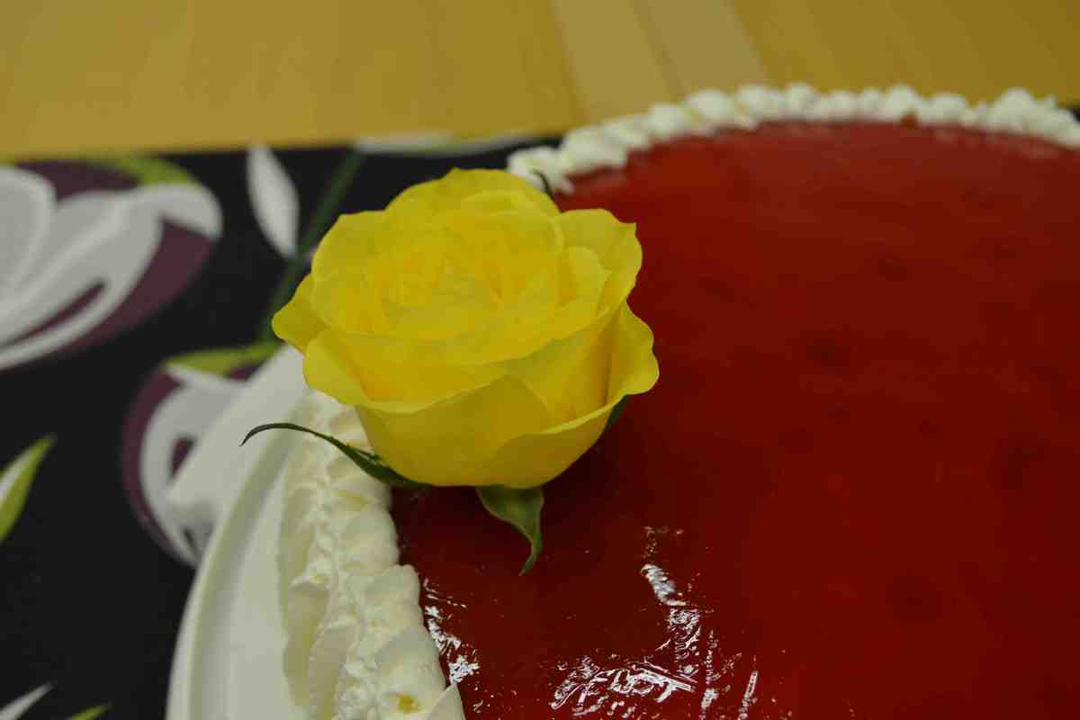 Keltainen ruusu täytekakun punaisen kiillekerroksen päällä